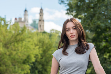 Beautiful Ukrainian caucasian girl with red hair, blue eyes and freckles in a grey dress posing and smiling with green trees and a church on background