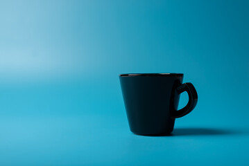 A black cup on a blue background. Cup minimalism