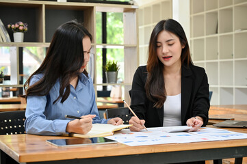 Beautiful young Asian female financial manager training her new staff in the office.