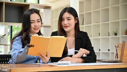 Asian businesswomen working together in the office, looking for information in a book.