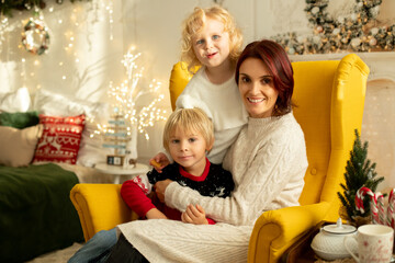 Cute little toddler curly girl in winter christmas sweater, sitting in cozy room, decorated for christmas