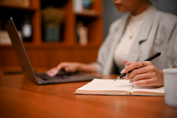 cropped, Female boss working at her desk, using laptop and writing something on notebook.
