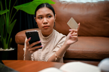 Gorgeous young Asian female holding a smartphone and a credit card, transferring money