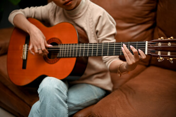cropped image, A gorgeous young Asian female playing guitar in her home living room.