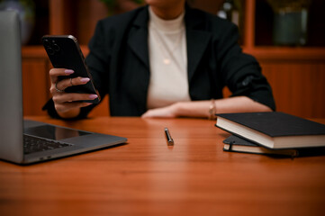 Professional Asian businesswoman in black suit using her smartphone at her office desk.