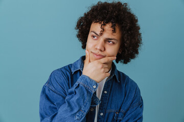 Fototapeta na wymiar Curly young man wearing shirt holding his chin while looking aside