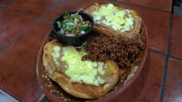 Mexican breakfast consisting of molletes which is toasted bread with beans, cheese, machaca meat and gallo sauce to accompany