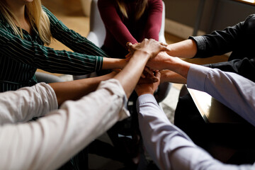 Positive diverse business team putting their hands on top of each other, showing unity and teamwork