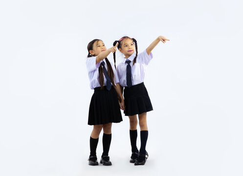Back to school concept. Junior school asian cute international student in uniform posing finger pointing on white background.