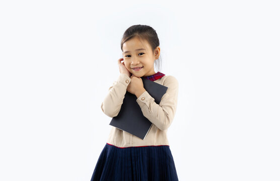 Asian schoolgirl holding book looking camera standing and posing on white wall background.