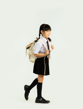 Back to school. Asian junior school student in british international uniform carrying backpack walking white background.