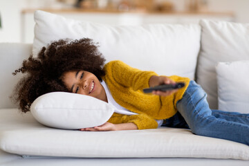 Happy black school girl lying on couch, watching TV