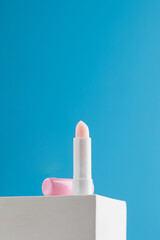 Pink moisturizing hygienic lipstick on a podium on a blue background. Place for advertisement.