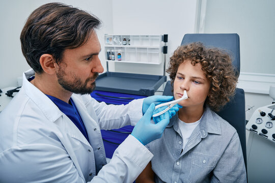 ENT using nasal speculum or rhinoscope to examine child patient's nose area. Curly boy while rhinoscopy in medical clinic