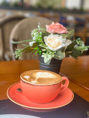 Red cup of cappuccino next to a bouquet of flowers