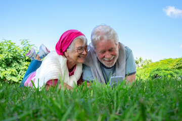 Portrait of senior smiling couple lying on the grass in public park looking at mobile phone together. Romantic couple enjoying free time and retirement