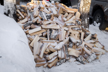 A bunch of chopped birch logs in the snow. Firewood for heating the house in winter. Fuel for the fireplace and stove in the house. Selective focus