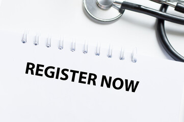 REGISTER NOW text on a notebook on a table with a stethoscope