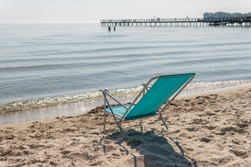 Fototapeta na wymiar A folding chair on the beach facing the sea. Warm sunny day. Symbol of holidays, leisure.