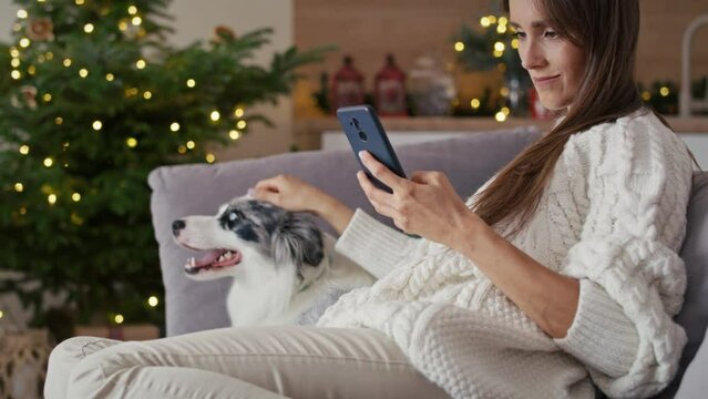Woman chilling with dog on sofa with mobile phone during the Christmas. Shot with RED helium camera in 8K.  