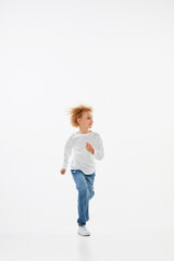 Full-length portrait of little girl, kid in white long sleeve blouse and jeans running isolated over white background. Fashion, happy childhood