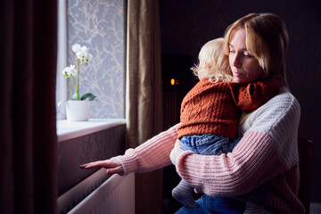Mother With Son Trying To Keep Warm By Radiator At Home During Cost Of Living Energy Crisis - obrazy, fototapety, plakaty