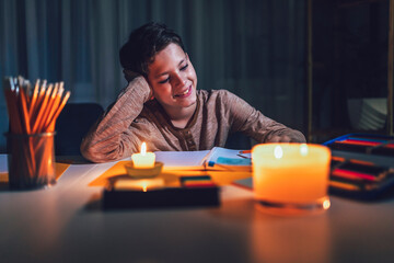 Little boy studying in low light with a burning candle.  Power outage, energy crisis concept.