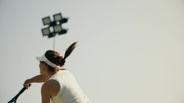 4k video female tennis player in white serving. Young woman hit the tennis ball with racket. Tennis serve on sky background.