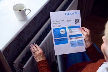 Close Up Of Senior Woman In Wheelchair With Energy Bill By Radiator In Cost Of Living Energy Crisis