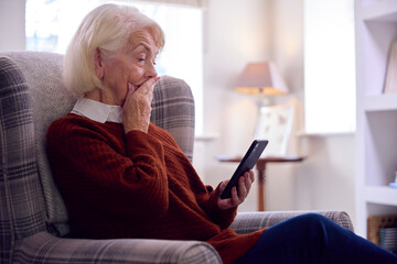Worried Senior Woman With Mobile Phone Keeping Warm By Portable Radiator In Cost Of Living Crisis