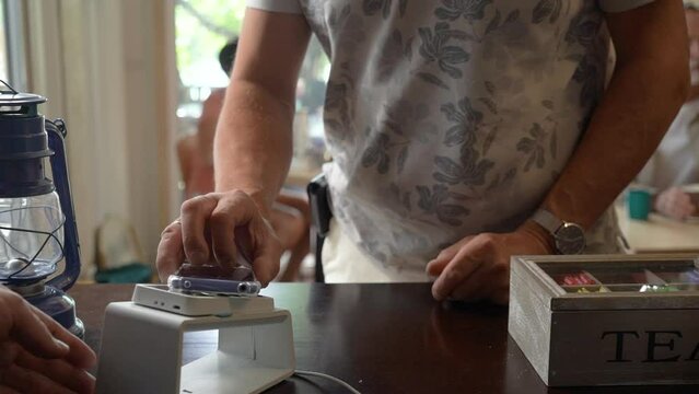 An elder male customer pay the bill via a smartphone using NFC contactless technology in a cafe. Purchase by cell-phone on electronic payment machine or card reader. E-money at cashless wallet.