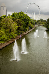 Singapore, July 24, 2022 - Water fountains on canal with ferris wheel in background.