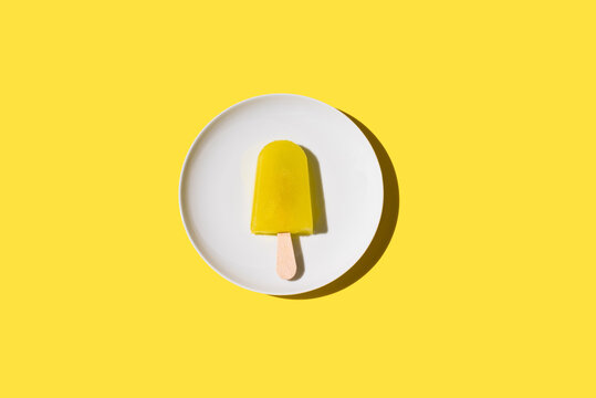 Polo de hielo sabor limón. Palo de helado sobre fondo amarillo y blanco. Concepto de verano. Vista superior