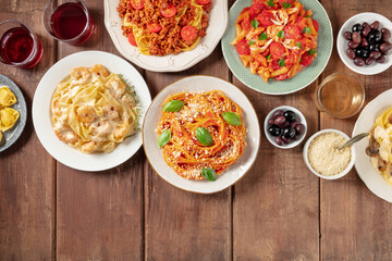 Italian food and drinks. Various pastas, olives, wine, grated Parmesan cheese, overhead flat lay shot on a rustic background with copy space