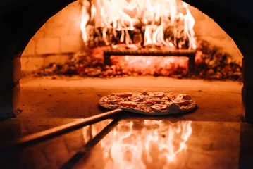 Foto op Aluminium The chef puts the Margherita, four cheese or meat pizza on a shovel in the oven. A firewood oven for cooking and baking pizza. Italian traditional pizza is cooked in a stone wood-fired oven. © Serhii
