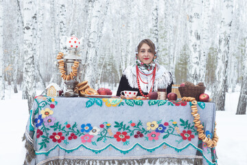 A girl in a winter forest. A beautiful woman in a fur coat at a covered table among the birches