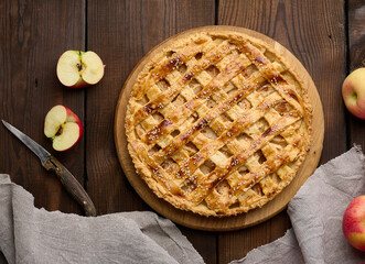 Round baked pie with apple filling on a wooden board, brown table.
