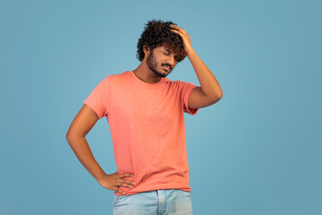 Uspet indian guy touching his head, blue background
