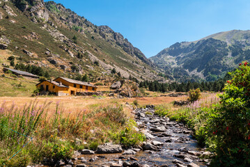 Incles valley in Andorra, surrounded by mountains with a river running through the valley and a house on a blue sky day