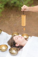 Male hand holding a bamboo Koshi chime during sound healing therapy with tibetan singing bowls over young woman outdoor