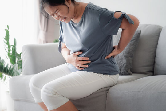 Woman suffering from stomachache sitting on the sofa at home. abdominal pain, Gastritis, Period, menstruation.
