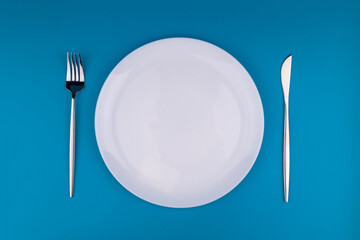 Stylish table setting, empty white plate with fork and knife on blue background, top view, flat lay