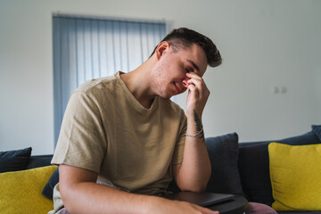 A young man having head back and neck pain in his home office while sitting on the couch during the day