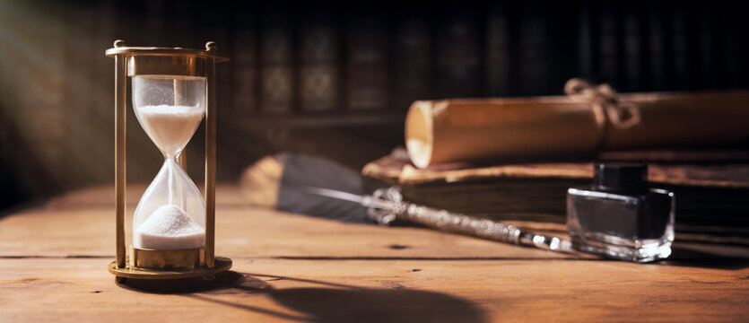 Sand Running Through The Hourglass On Old Wooden Table With Vintage Books And Quill Pen. Time Is Ticking. Banner