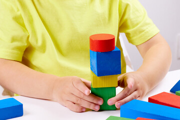 A child plays with playful colored geometric shapes on a light table. The child builds towers from toy building bricks. selective focus