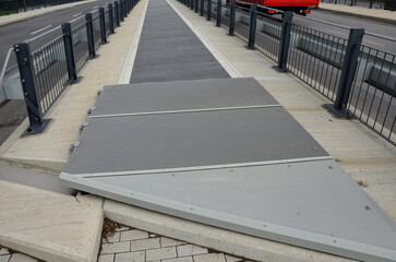 the space between the lanes of the highway bridge is blocked by a grid. the guardrails are in combination with the black metal railing bolted to the concrete bridge, tension rod