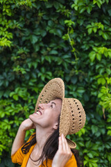 A smiling girl in a straw hat stands near a wall overgrown with ivy