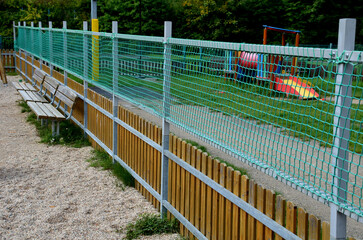 fencing of the children's playground with an additional net above the wooden fence. the galvanized metal frame increases the height of the fence with a green textile mesh. sandbox