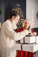 Senior man presenting christmas gift to his wife standing near christmas tree