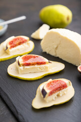 Summer appetizer with pear, cottage cheese, figs and honey on a black concrete background. Side view, selective focus.